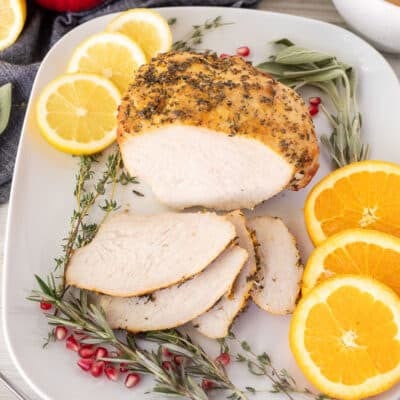Sliced Turkey Breast Roast on a platter with citrus slices and herbs.