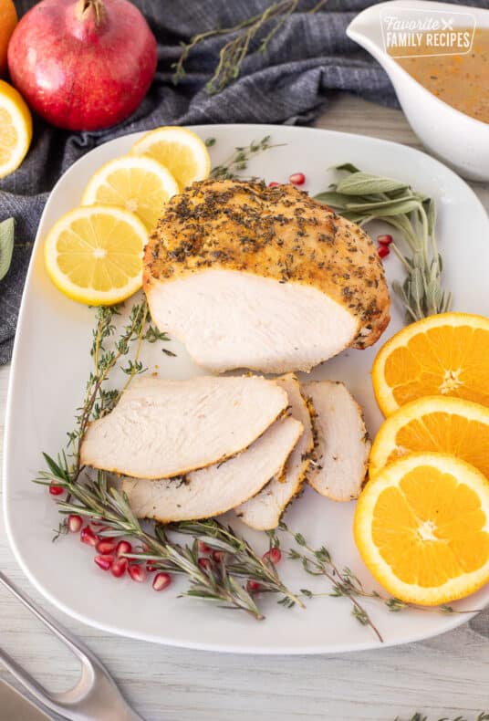 Sliced Turkey Breast Roast on a platter with citrus slices and herbs.
