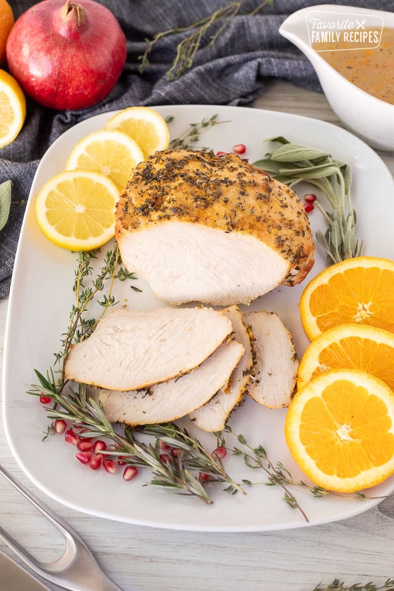 Sliced Turkey Breast Roast on a platter with citrus slices and herbs.