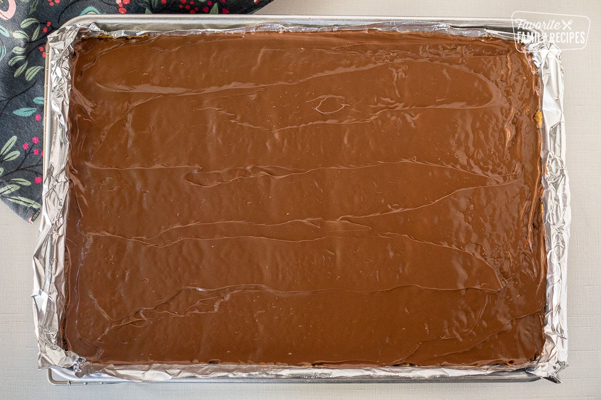 Smooth melted chocolate on top of Christmas Crack Candy in a baking sheet.