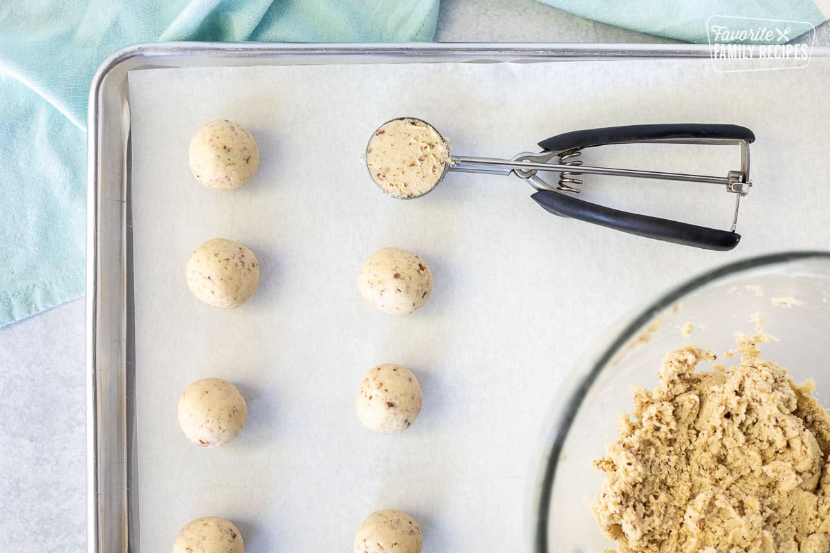 Cookie scoop on parchment lined cookie sheet with balls of Snowball cookie dough.