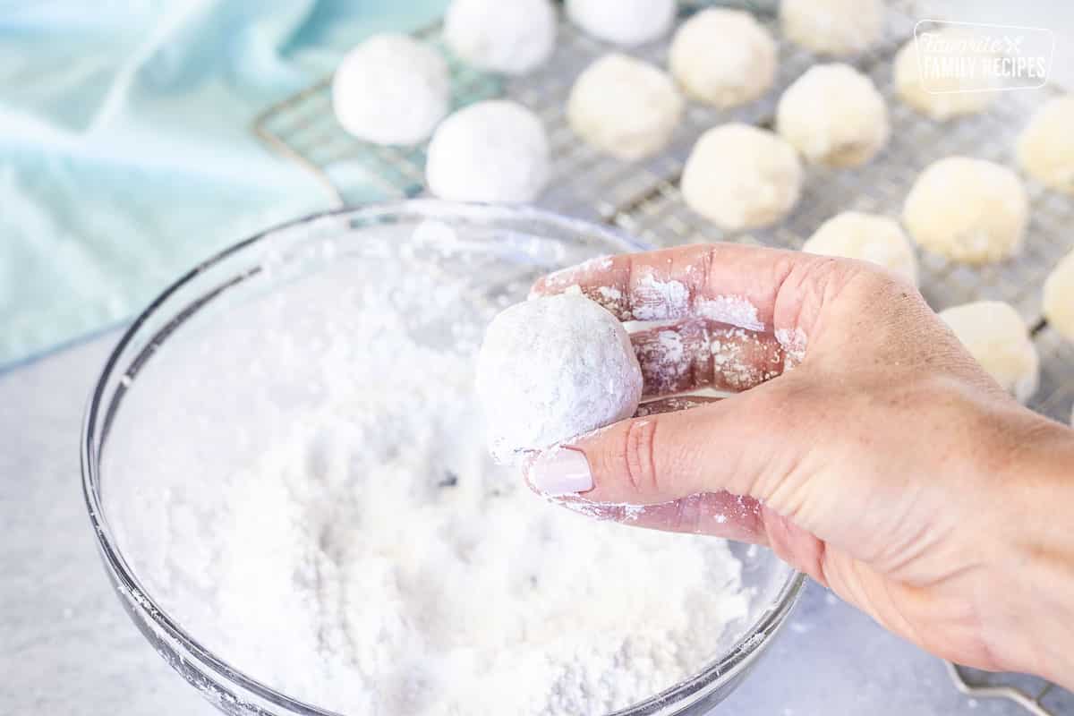 Hand second dipping Snowball Cookies in bowl of powdered sugar.