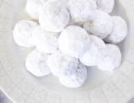 A white tray filled with snowball cookies and a dish of sprinkles on the side.