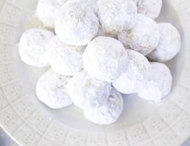A white tray filled with snowball cookies and a dish of sprinkles on the side.