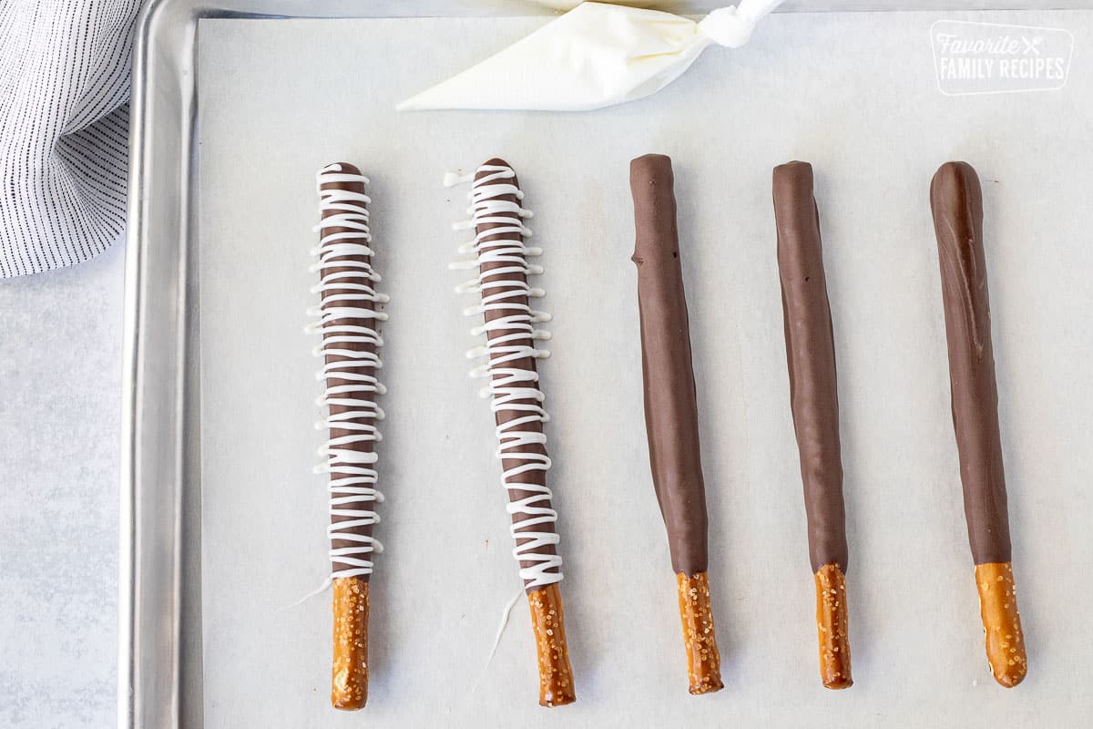 Swirl chocolate pattern on the pretzel rods. Small piping bag of melted chocolate next to pretzel rods.
