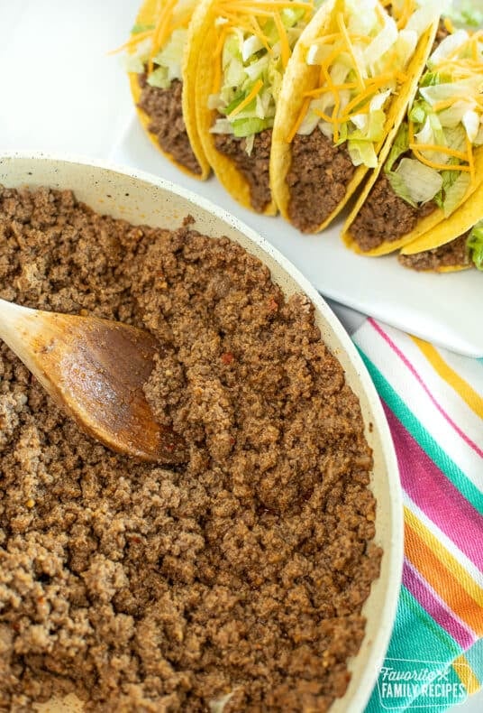 A skillet of Taco Bell meat with a wooden spoon scooping some of the meat