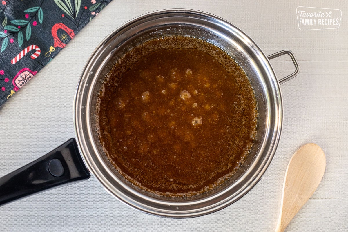 Pot of boiling caramel mixture next to wooden spoon.