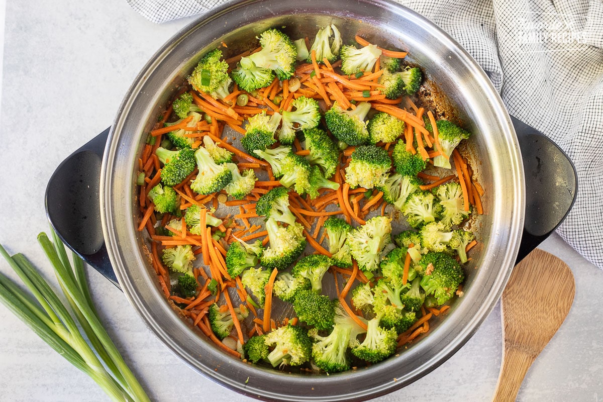 Skillet with cooked broccoli, carrots and green onion.