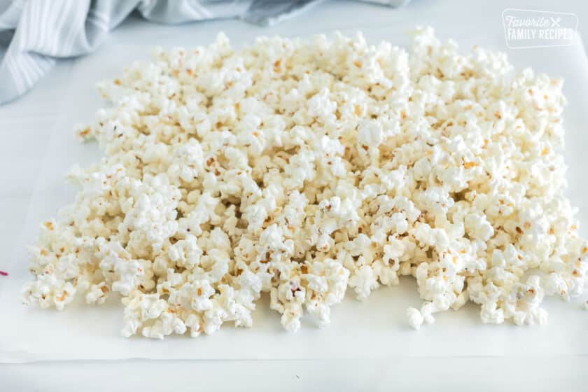 Popcorn that has been mixed with melted white chocolate is laid out on wax paper to cool and harden.