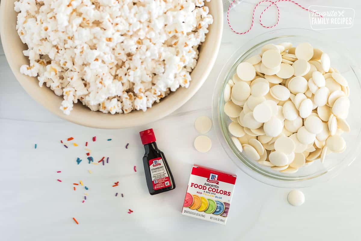 Ingredients for White Chocolate Popcorn, including white microwave popcorn, white chocolate candy melts, strawberry extract and food coloring.