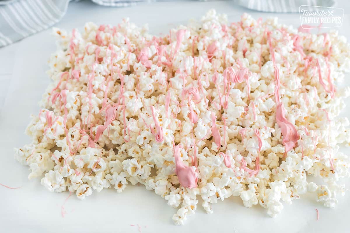 White chocolate popcorn laid out on wax paper after being garnished with ribbons of pink chocolate that is slowly cooling on top.