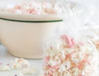 Vertical view of bags and a bowl of white chocolate popcorn. The popcorn has ribbons of melted pink chocolate across the pieces.