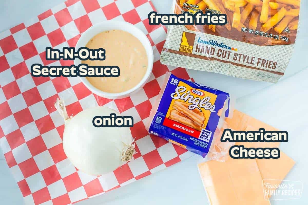Ingredients to make animal style fries on a table including cheese, onion, fries, and sauce.