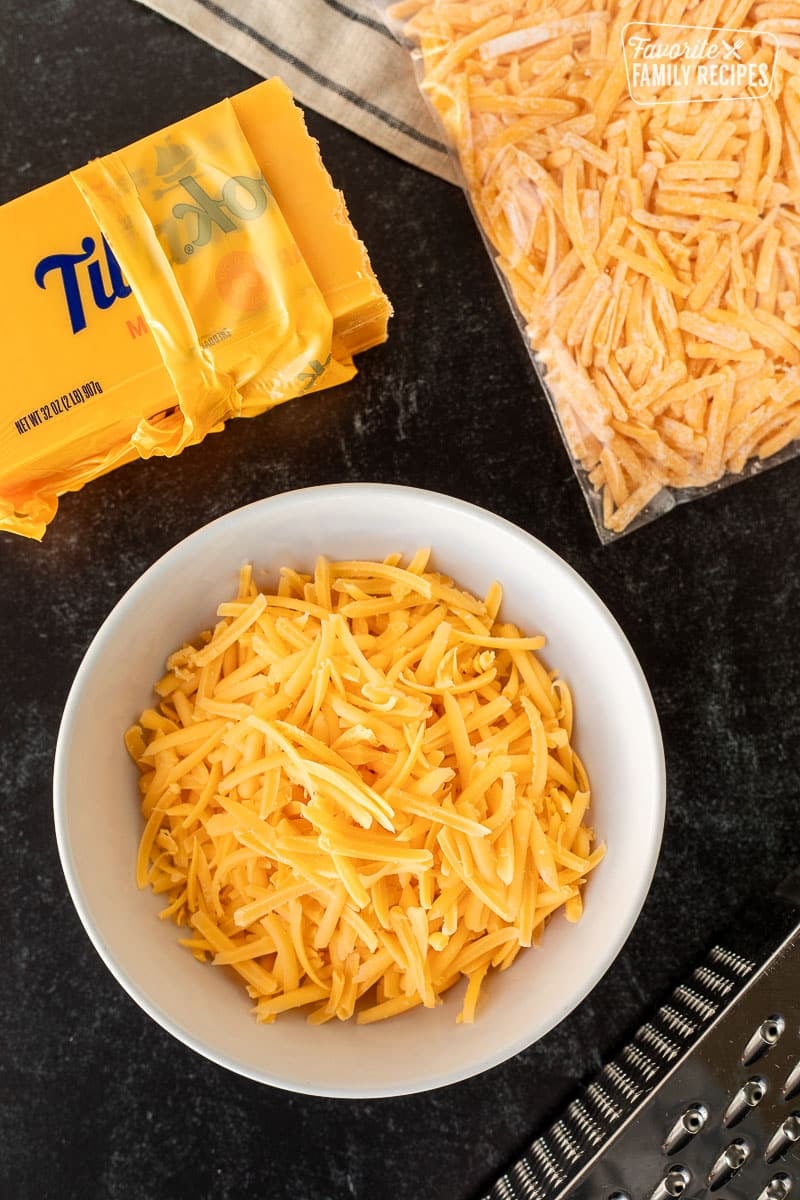 Bowl of grated cheddar cheese next to bag to freeze cheese and block a of cheddar cheese.