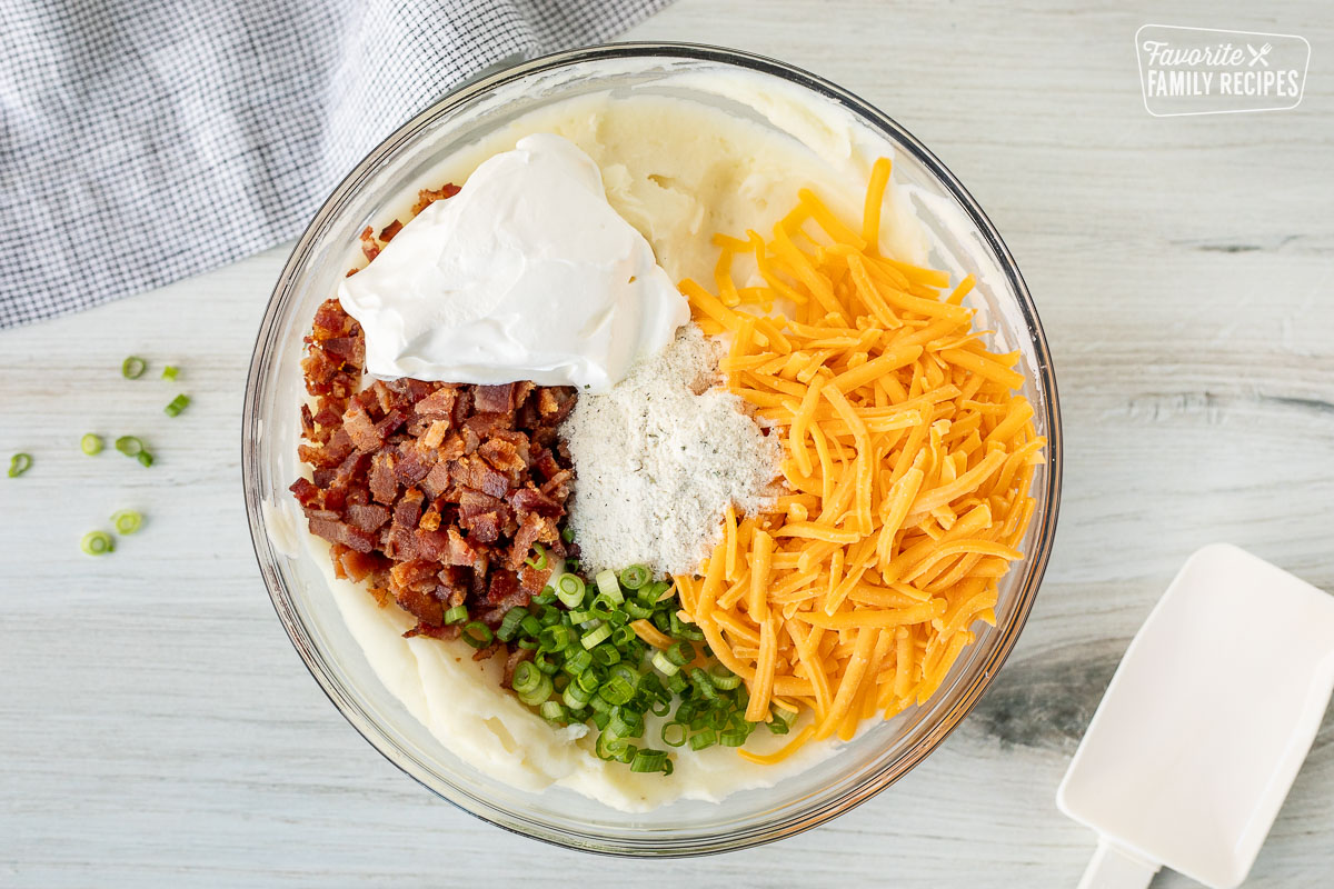 Mixing bowl with mashed potatoes, shredded cheddar cheese, sliced green onions, chopped bacon, sour cream and Ranch dressing seasoning.