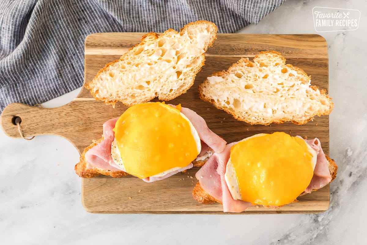Two croissants on a cutting board topped with ham, egg and cheese.