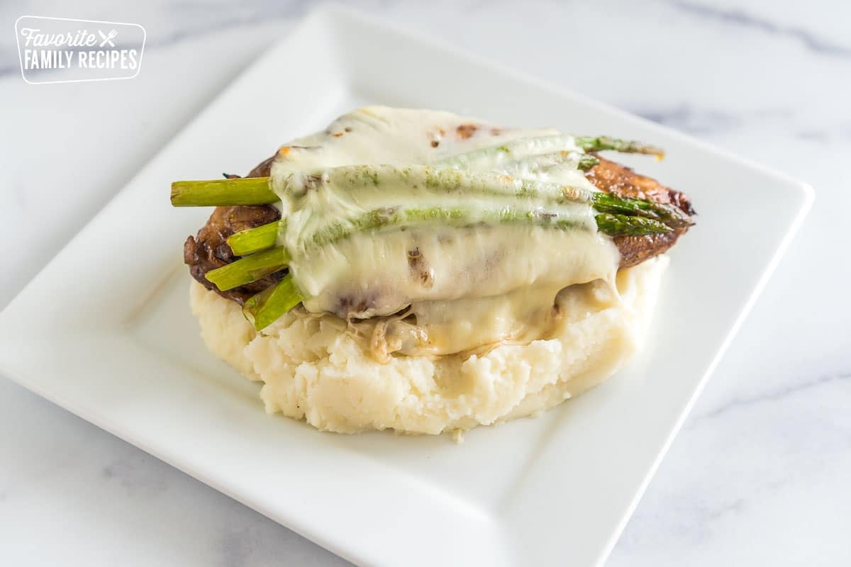 A pile of mashed potatoes with a chicken breast on top with melted cheese and asparagus.