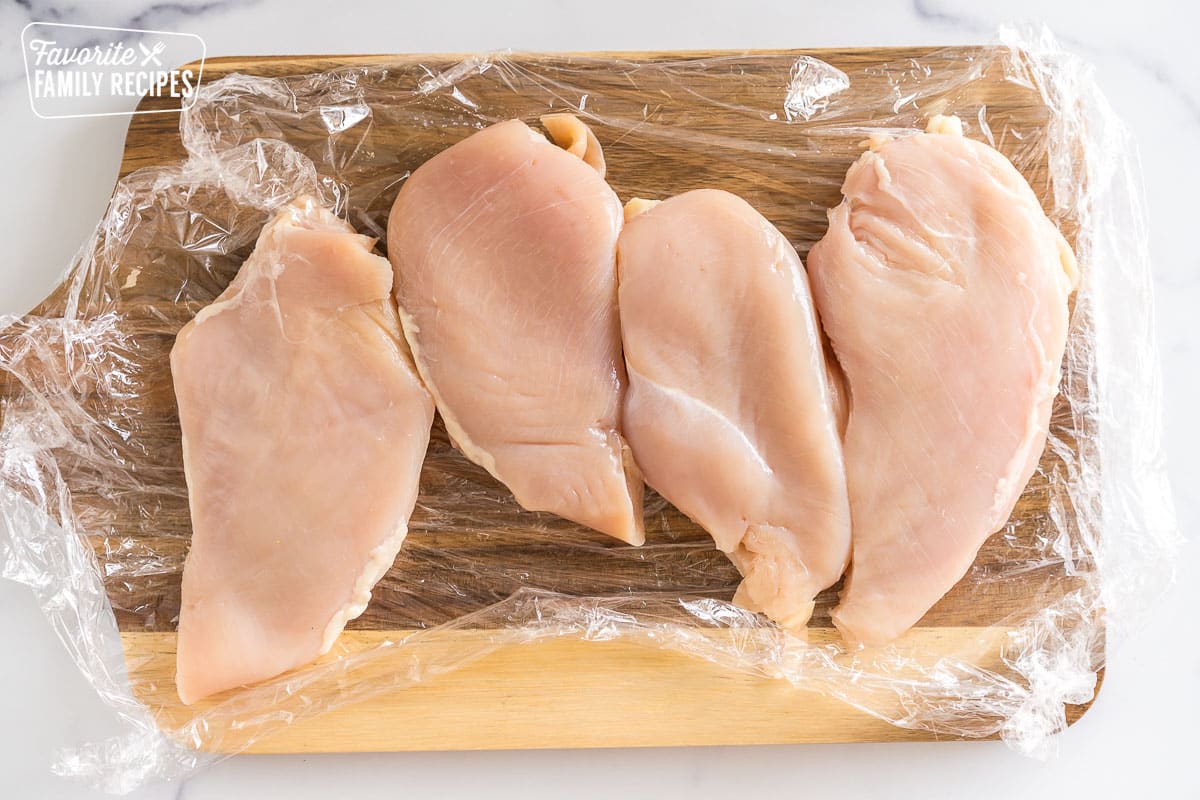 four chicken breasts on a cutting board, pounded thin