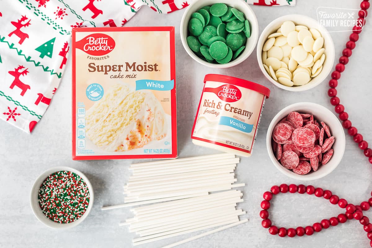 Ingredients to make Christmas Cake Pops including white cake mix, sprinkles, vanilla frosting, lollipop sticks, green candy melts, red candy melts and white candy melts.