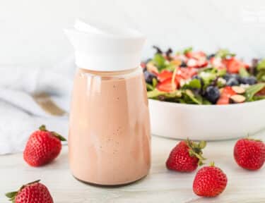 Salad dressing container of Strawberry Vinaigrette in front of a salad.