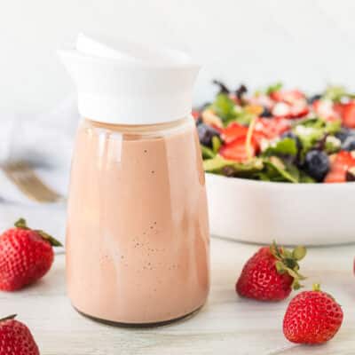 Salad dressing container of Strawberry Vinaigrette in front of a salad.