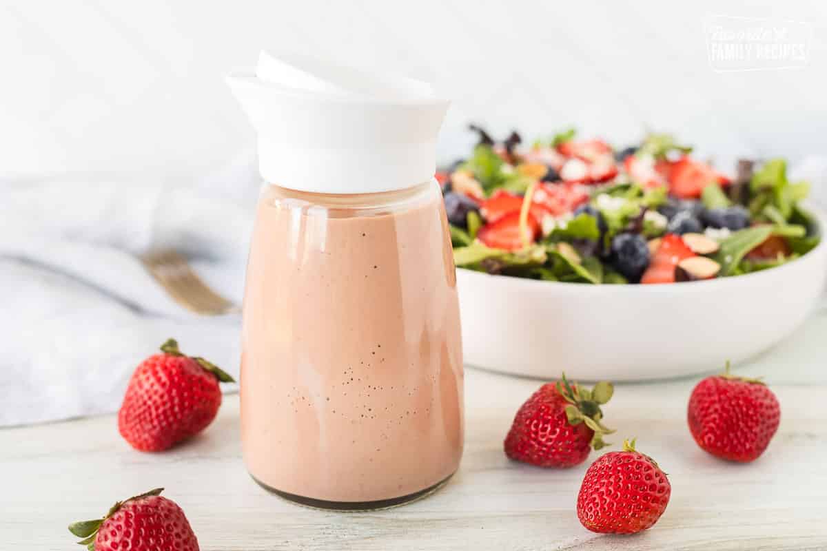 Salad dressing container of Strawberry Vinaigrette in front of a salad.