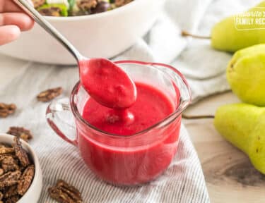 A small pitcher of pinkish red salad dressing with a spoon taking a spoonful