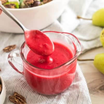A small pitcher of pinkish red salad dressing with a spoon taking a spoonful