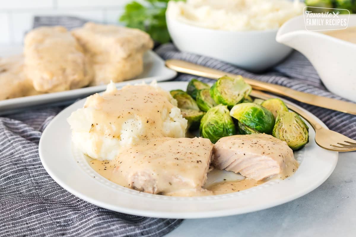 Cut Crock Pot Pork Chop on a plate with gravy. Mashed potatoes and brussels sprouts on the side.