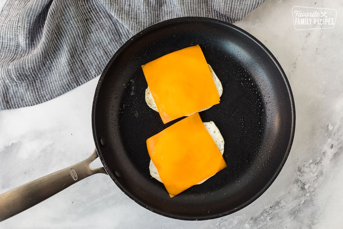 Two cooked eggs covered with cheese slices in a skillet.