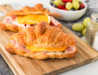 Two Croissant Breakfast Sandwiches on a cutting board with ham, egg and cheese.