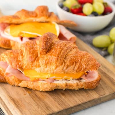 Two Croissant Breakfast Sandwiches on a cutting board with ham, egg and cheese.