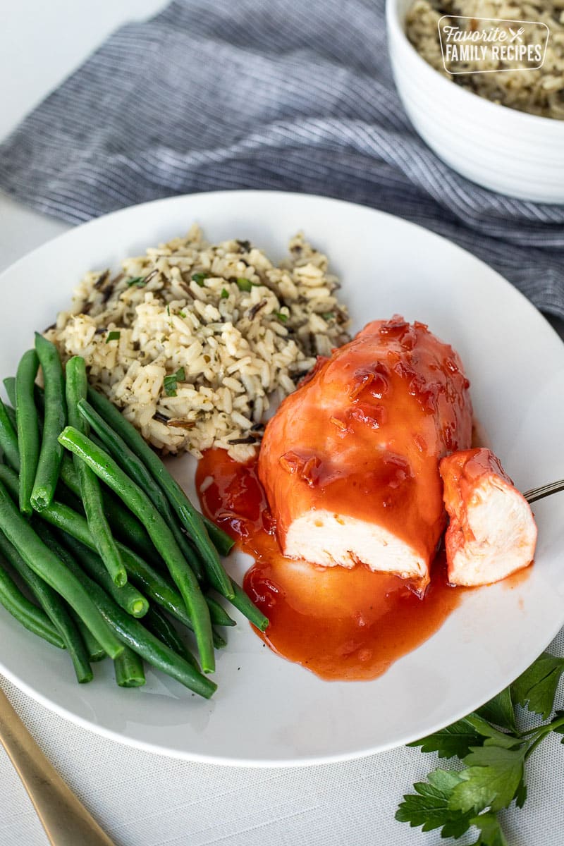 Plate with a piece of Apricot Chicken and a piece cut out. Green beans and rice on the side.