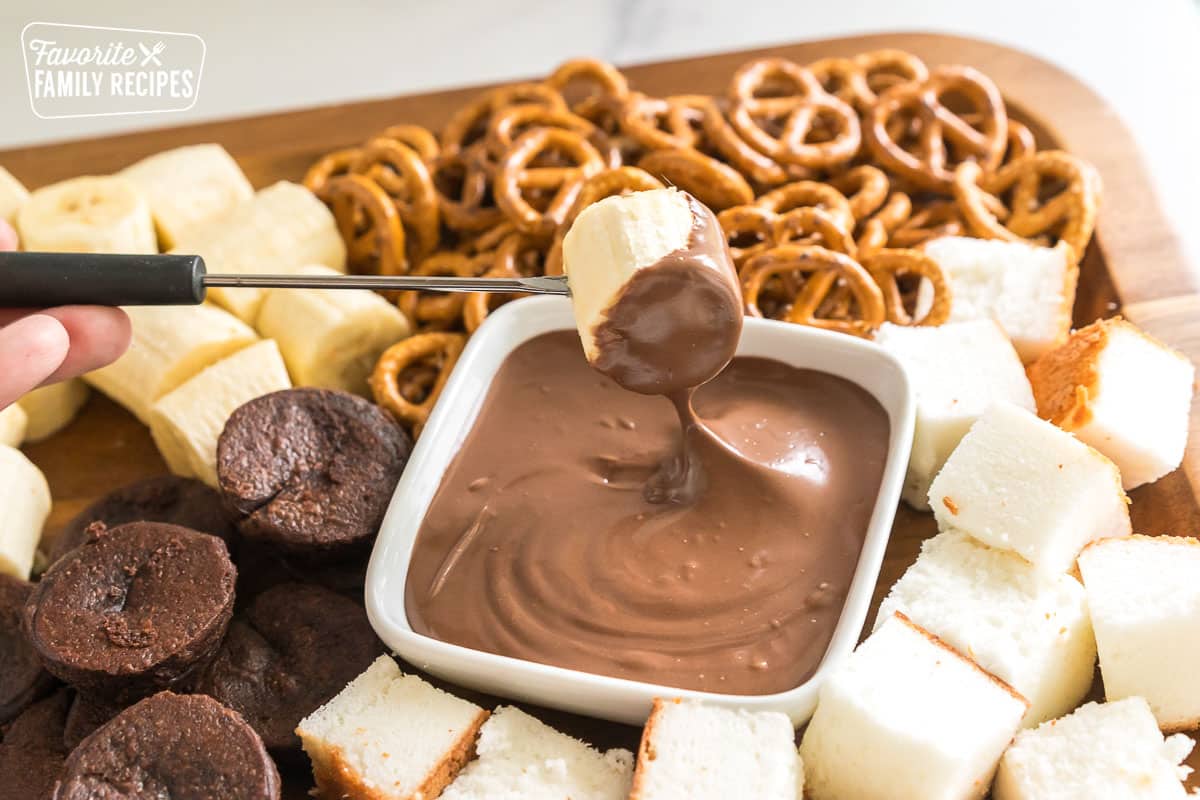 A fondue fork dipping a banana in milk chocolate.