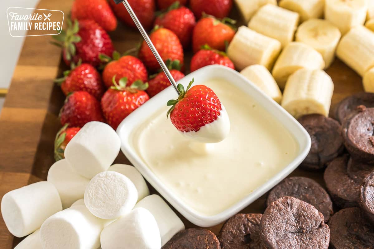 A fondue fork dipping a strawberry in white chocolate.