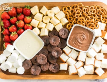 a charcuterie board with white chocolate, and milk chocolate and strawberries, pretzels, marshmallows, bananas, pound cake, and brownie pieces