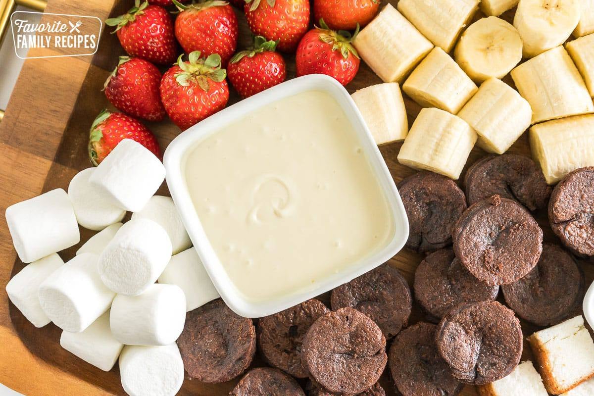 a bowl of melted white chocolate surrounded by fruits for a dessert charcuterie board.