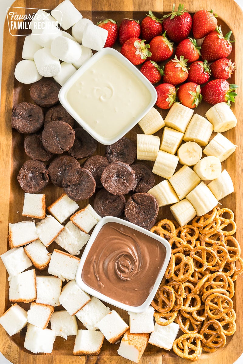 a charcuterie board with white chocolate, and milk chocolate and strawberries, pretzels, marshmallows, bananas, pound cake, and brownie pieces