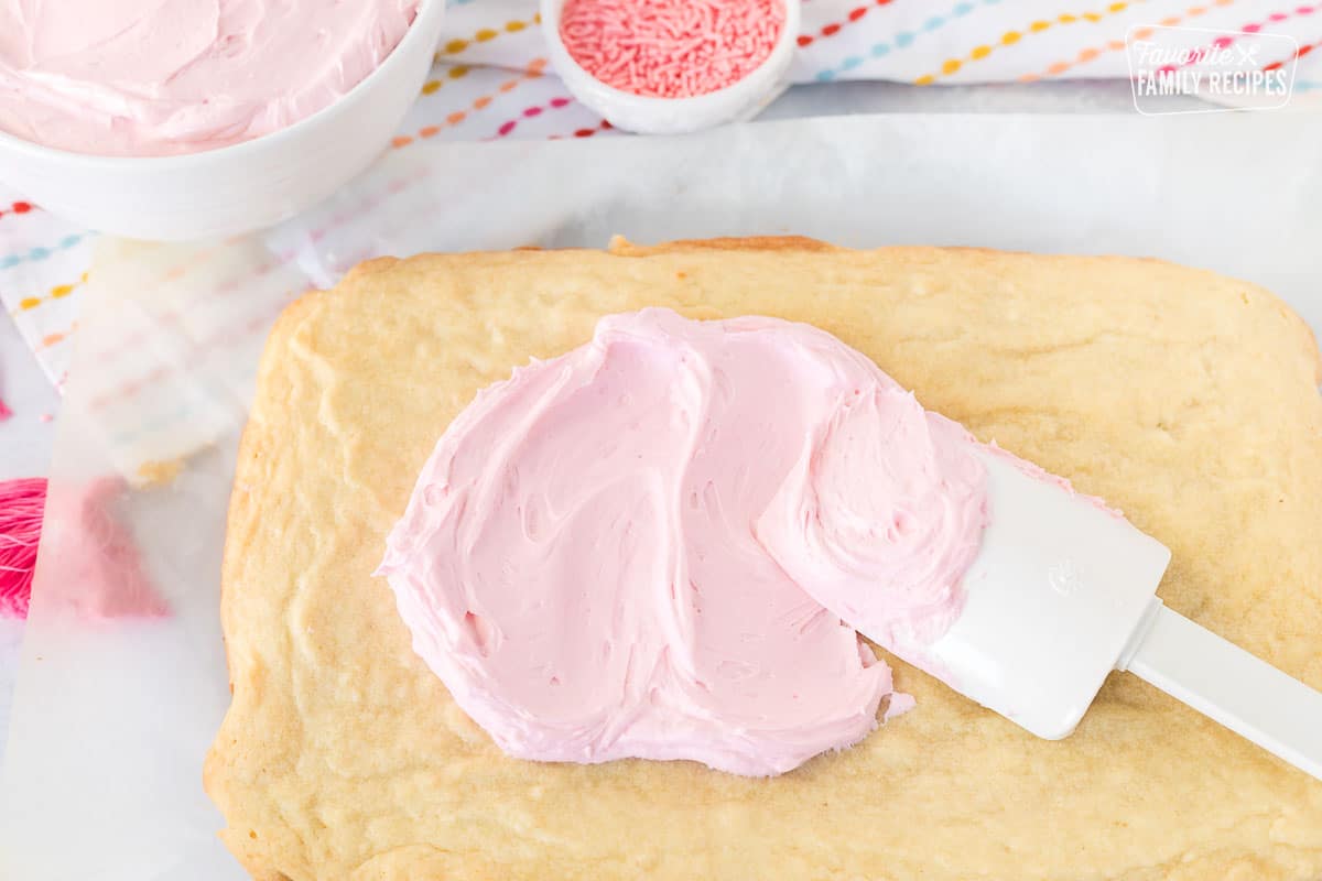 Spreading pink sugar cookie frosting onto a sugar cookie bar.
