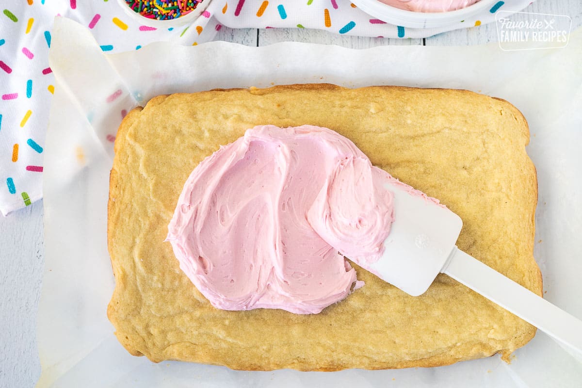 Spreading pink frosting onto sugar cookie bars.
