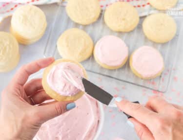 Spreading frosting on a pink Sugar Cookie.