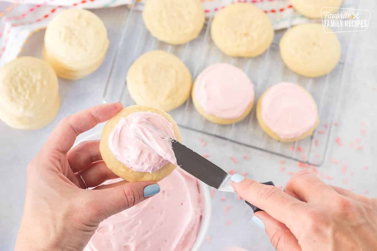 Spreading frosting on a pink Sugar Cookie.