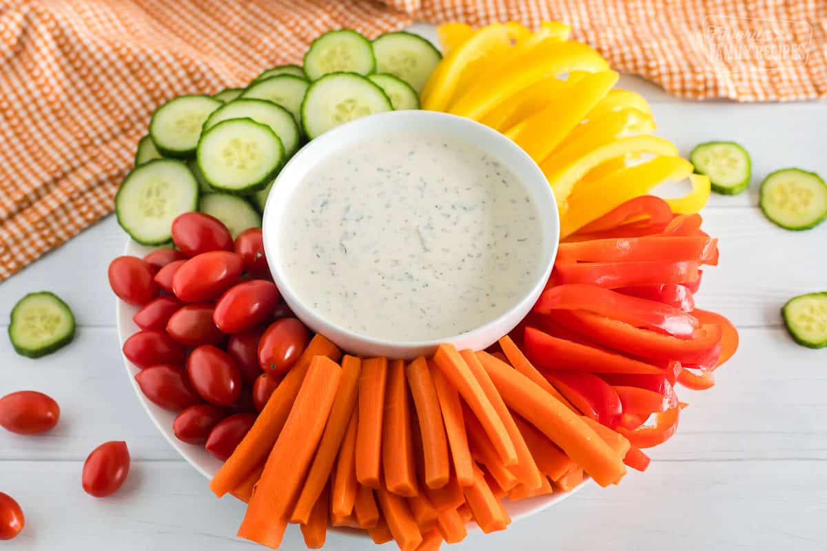 Homemade ranch dressing in a white bowl with sliced veggies around the outside.