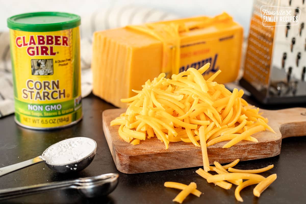 Grated cheddar cheese, grater, block of cheese and corn starch ingredients to freeze cheese.