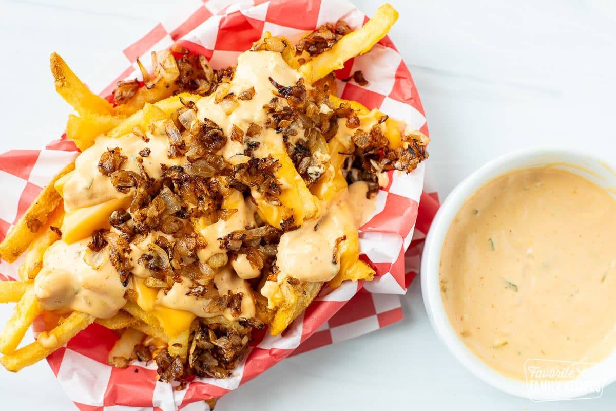 A basket of In N Out animal style fries next to a bowl of In N Out sauce