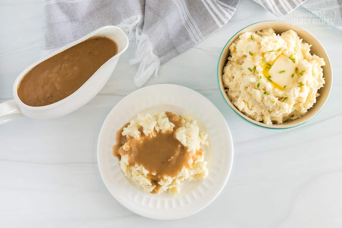 A gravy bowl, a white plate with mashed potatoes and gravy, and a side of mashed potatoes in a green bowl. 