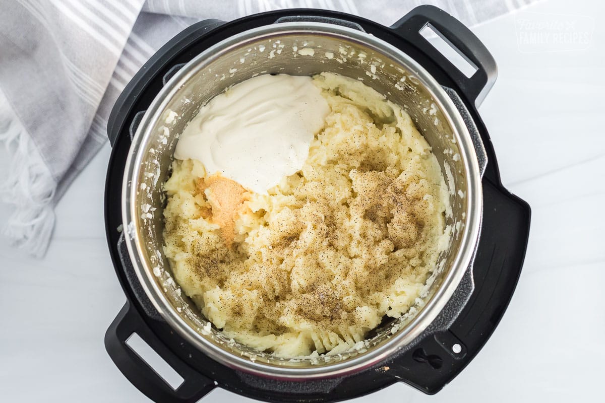 Instant pot mashed potatoes with sour cream and seasoning being ready to stir together.