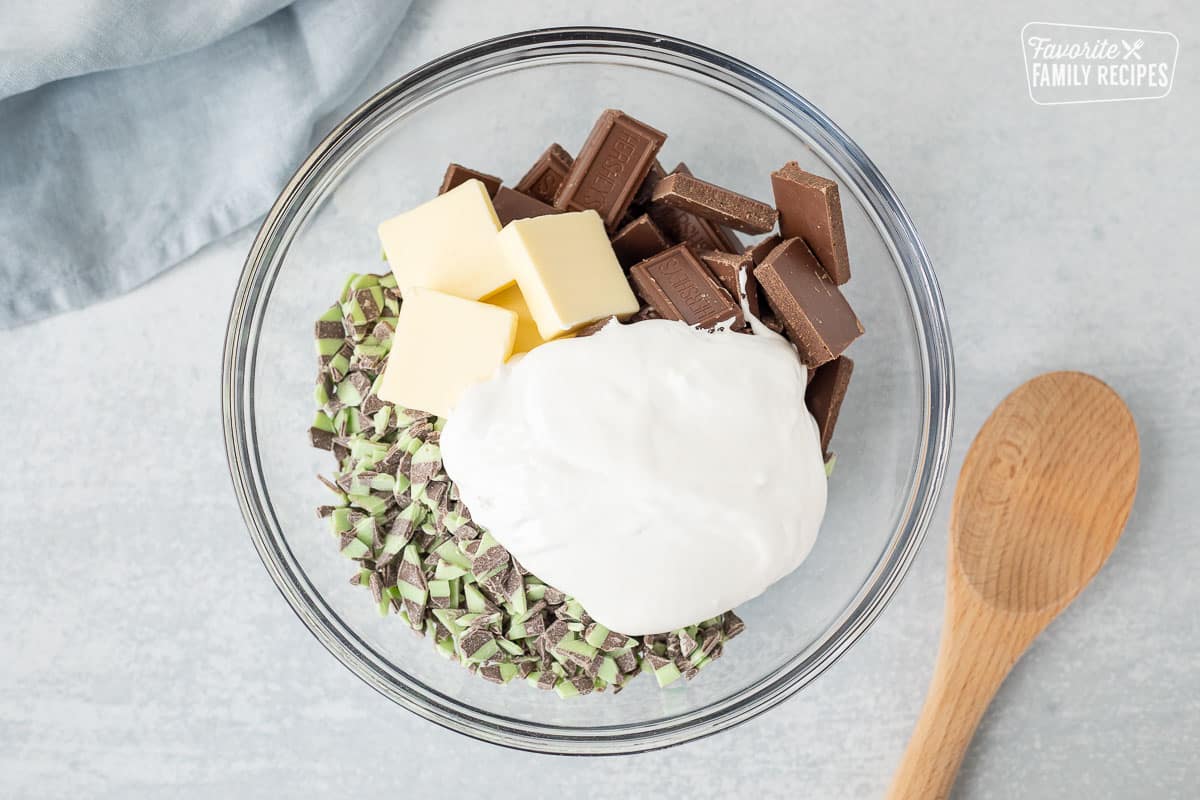 Bowl of mint chips, marshmallow creme, butter, chocolate pieces. Wooden spoon on the side.
