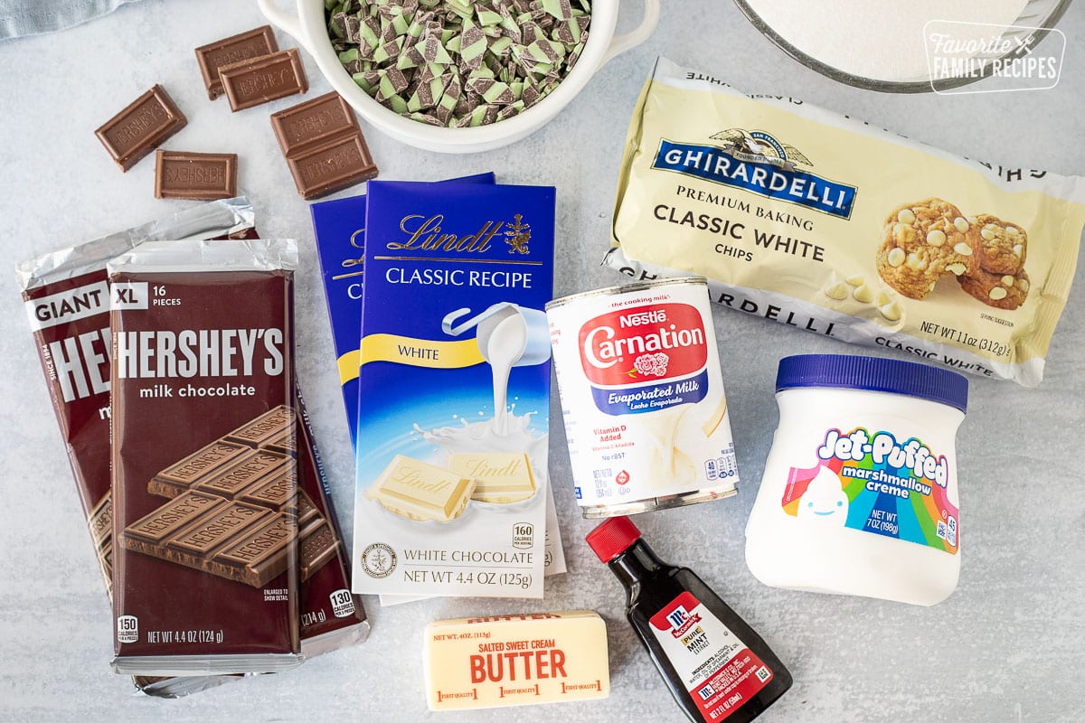 Ingredients to make Mint Chocolate Fudge including mint chips, white chocolate bars, chocolate bars, butter, sugar, evaporated milk, mint extract, marshmallow creme and white chocolate chips.