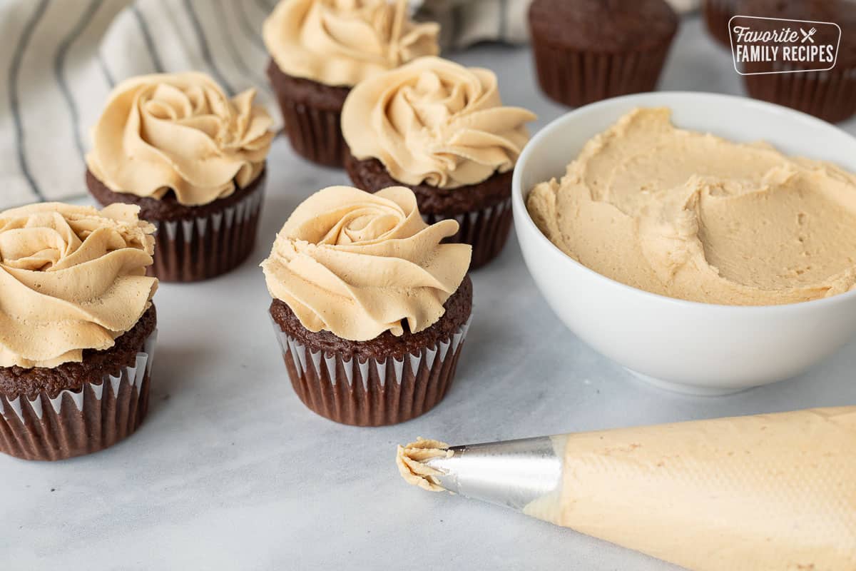 Piping bag with Peanut Butter frosting in front of chocolate cupcakes piped with Peanut Butter frosting.